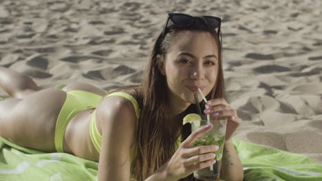 Glückliches-Mädchen-Im-Bikini,-Das-Am-Strand-Liegt-Und-Cocktail-Trinkt